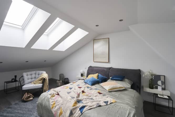 Chambre mansardée avec plafond en pente et fenêtres de toit VELUX, décoration chaleureuse.