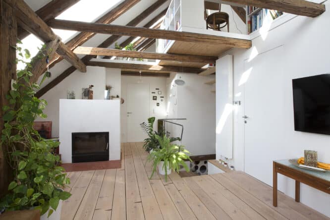 Espace habitable mansardé avec plafond incliné, fenêtre de toit VELUX et poutres apparentes.
