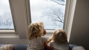Des enfants assis sur un canapé, regardant par une fenêtre de toit VELUX les arbres enneigés.