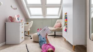 Enfant lisant un livre au sol dans une chambre mansardée sous une fenêtre de toit XXL.