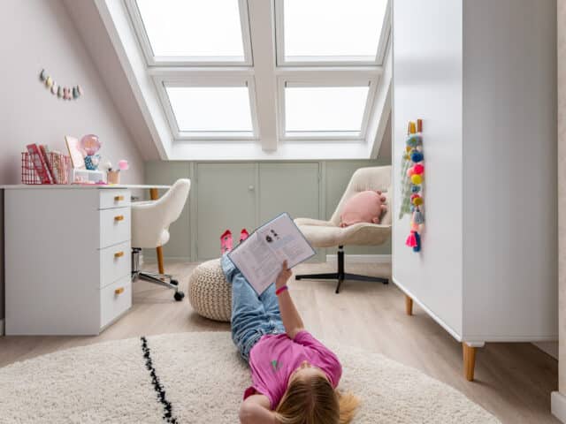 Enfant lisant un livre au sol dans une chambre mansardée sous une fenêtre de toit XXL.