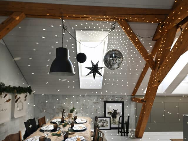 Salle à manger mansardée avec plafond en pente, poutres apparentes et décorations festives.