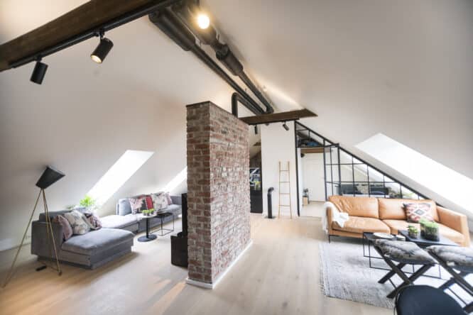 Salon mansardé avec plafond incliné, mur en briques apparentes et fenêtres de toit VELUX.
