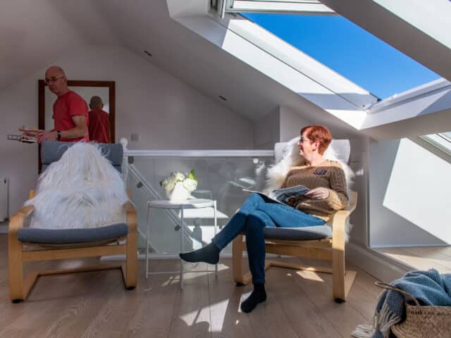 Chambre mansardée avec plafond incliné et fenêtre de toit VELUX, coin salon confortable.