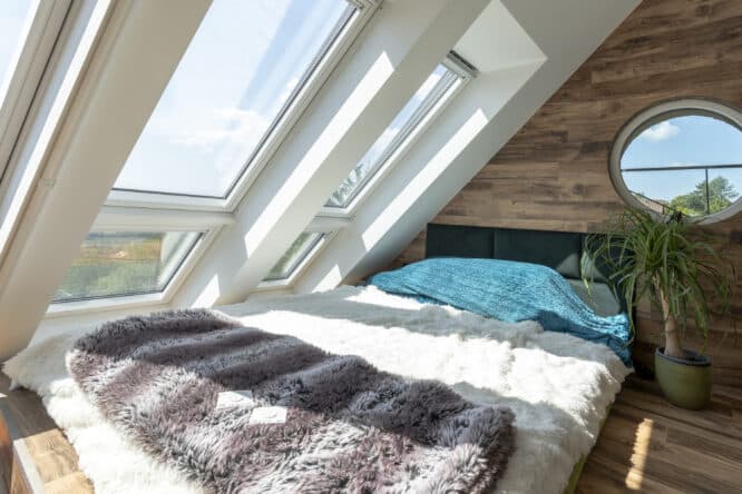Chambre mansardée avec fenêtres de toit VELUX et lit confortable.