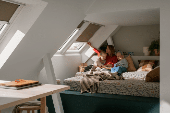 Chambre mansardée avec fenêtres de toit VELUX et store, coin nuit avec femme et filles, lumière naturelle.