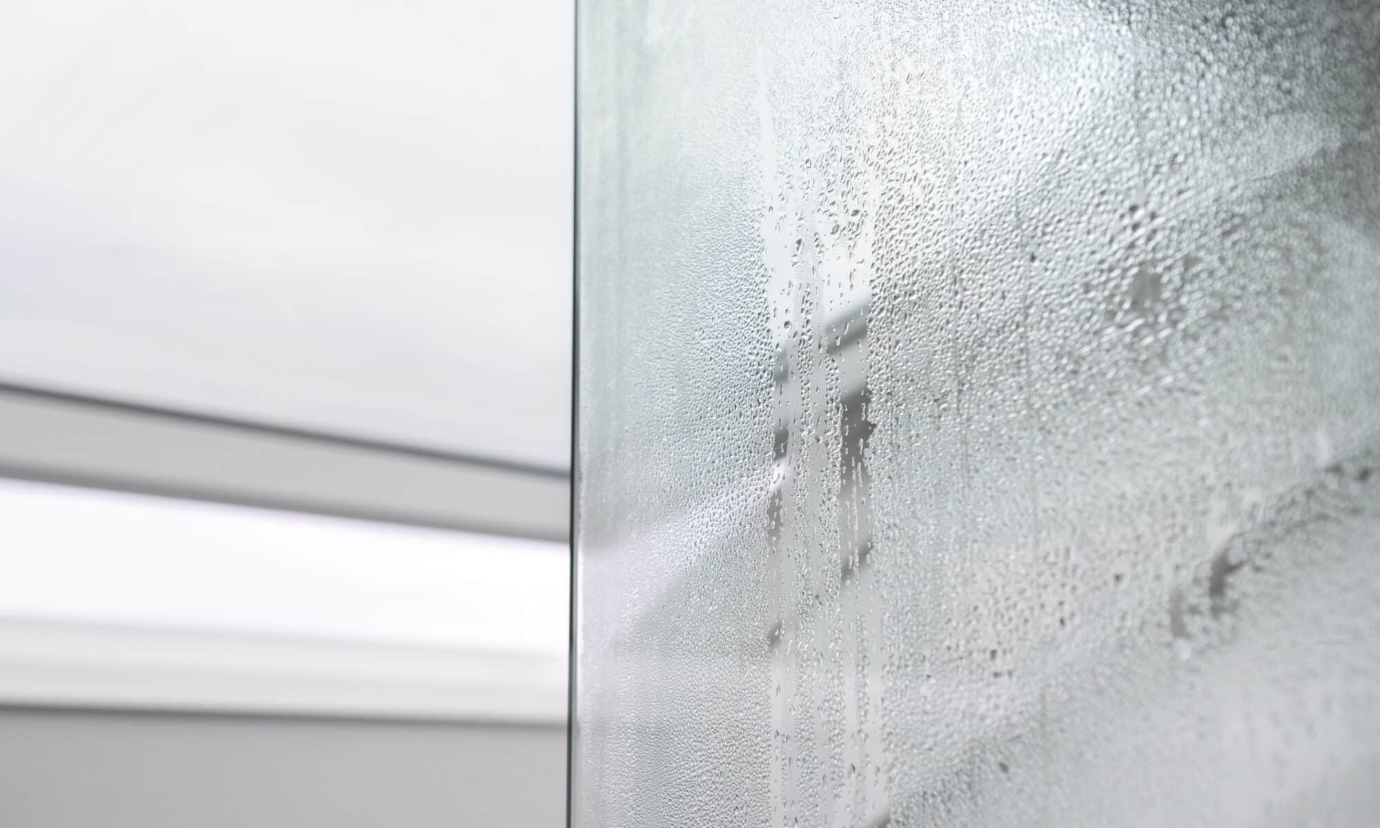 Gros plan sur des gouttelettes de condensation sur une surface en verre, créant un motif texturé.