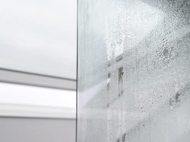 Gros plan sur des gouttelettes de condensation sur une surface en verre, créant un motif texturé.