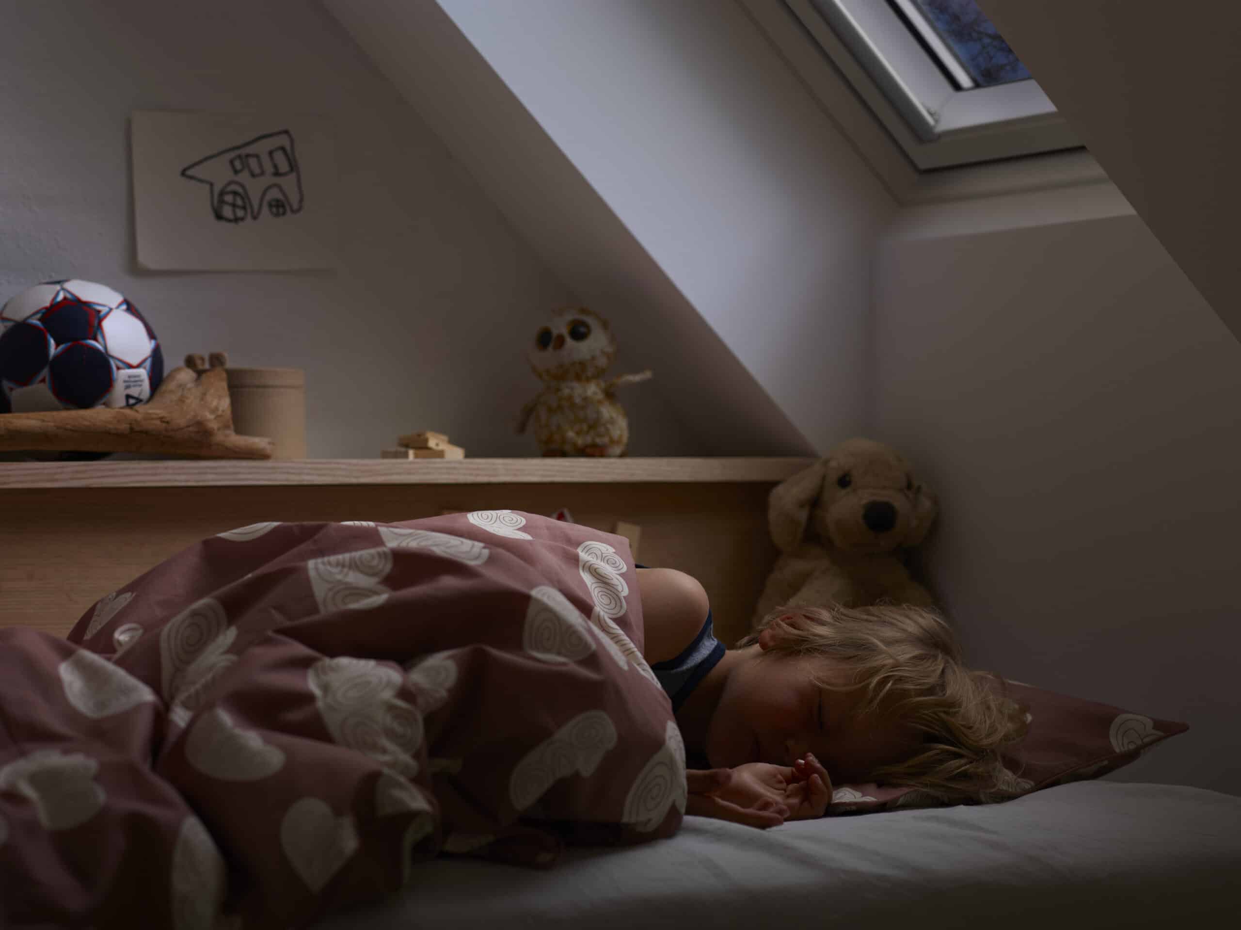 Enfant dormant dans une chambre mansard&eacute;e avec plafond en pente et fen&ecirc;tre de toit VELUX.
