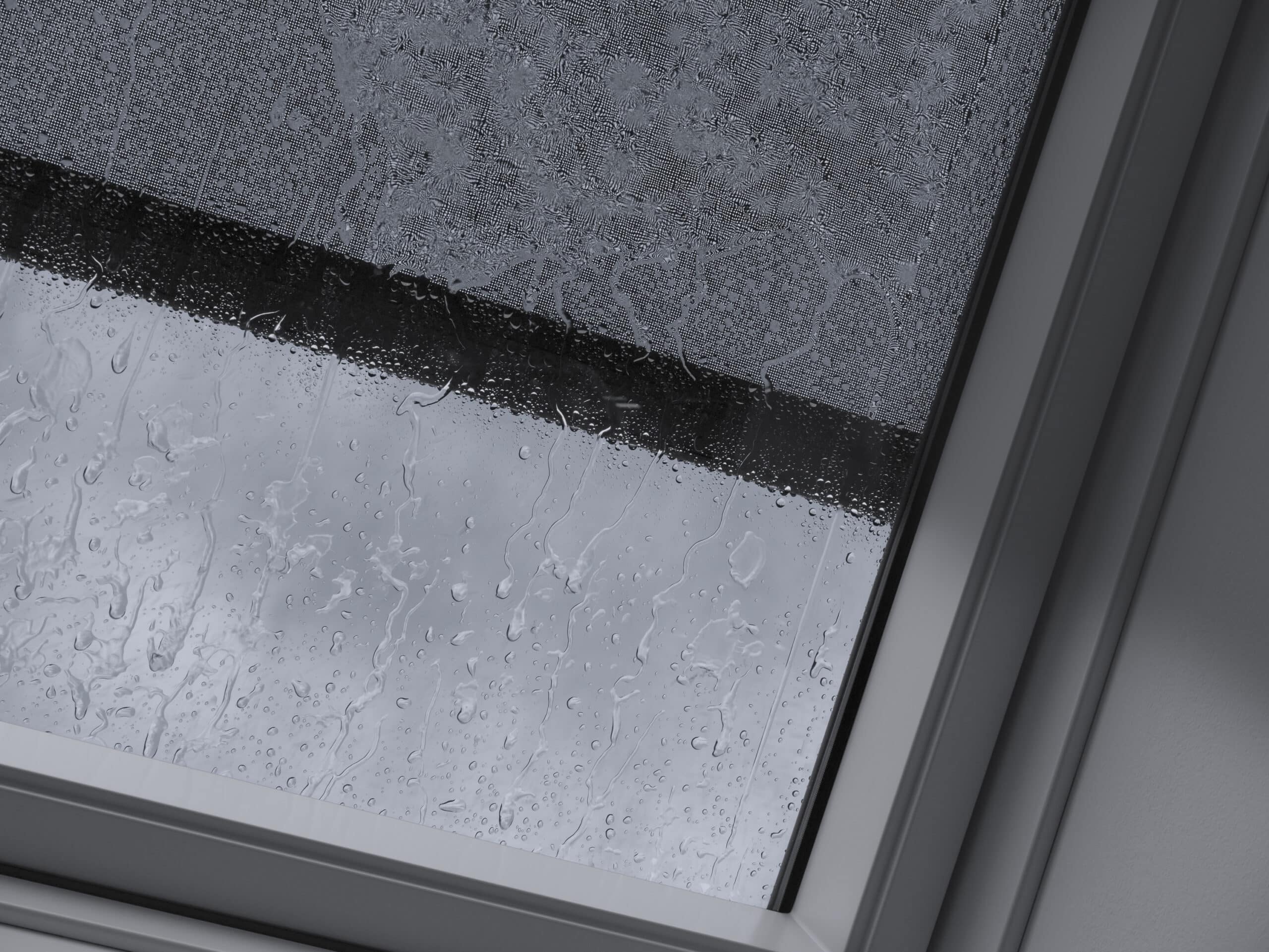 Fen&ecirc;tre de toit VELUX ferm&eacute;e avec des gouttes de pluie, vue sur un ciel pluvieux.