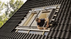 Ouvrier installant une fenêtre de toit VELUX sur un toit en tuiles noires à forte pente.