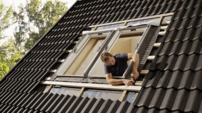 Ouvrier installant une fenêtre de toit VELUX sur un toit en tuiles noires à forte pente.