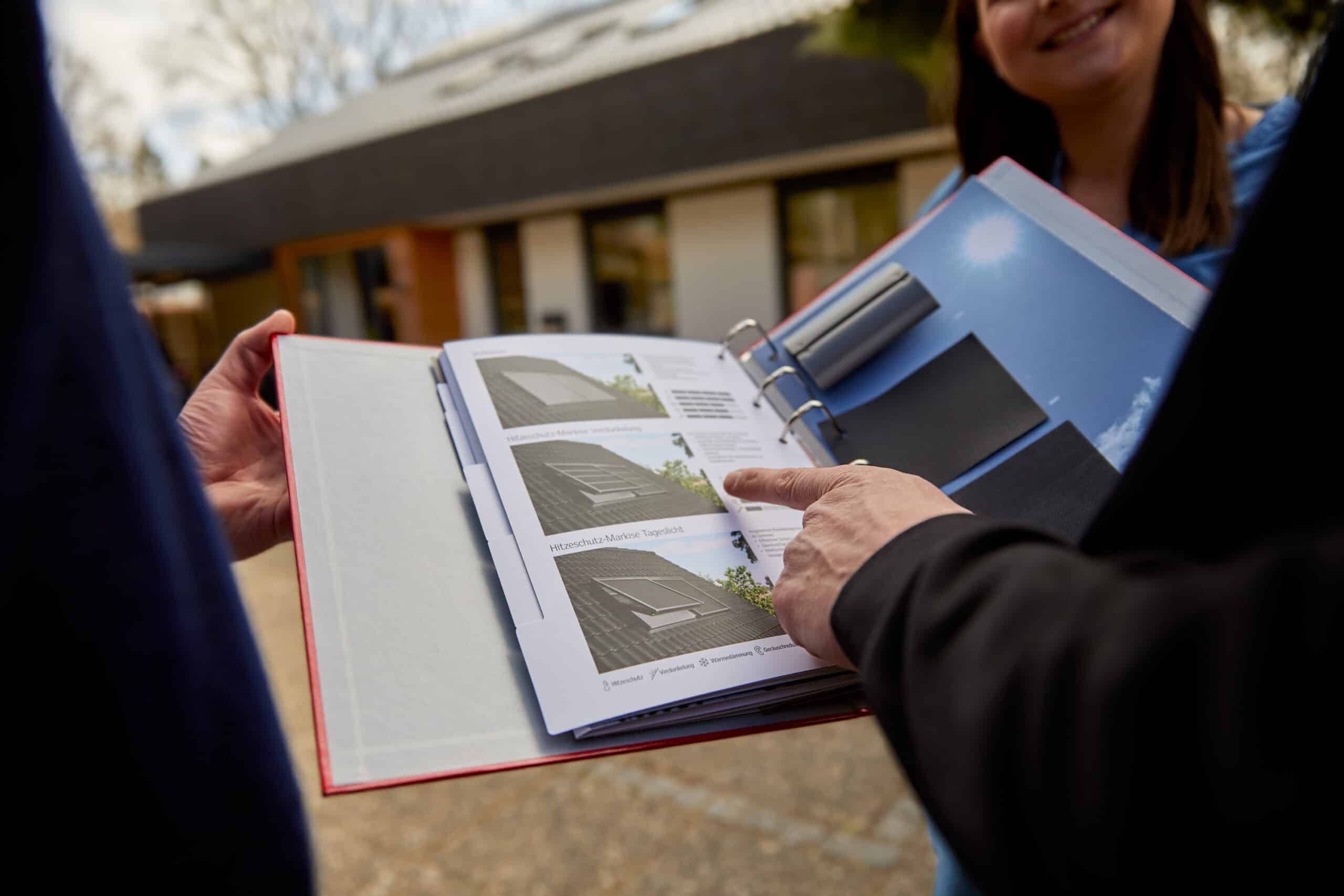 Deux personnes discutent des options de fen&ecirc;tres de toit pr&eacute;sent&eacute;es dans un catalogue.