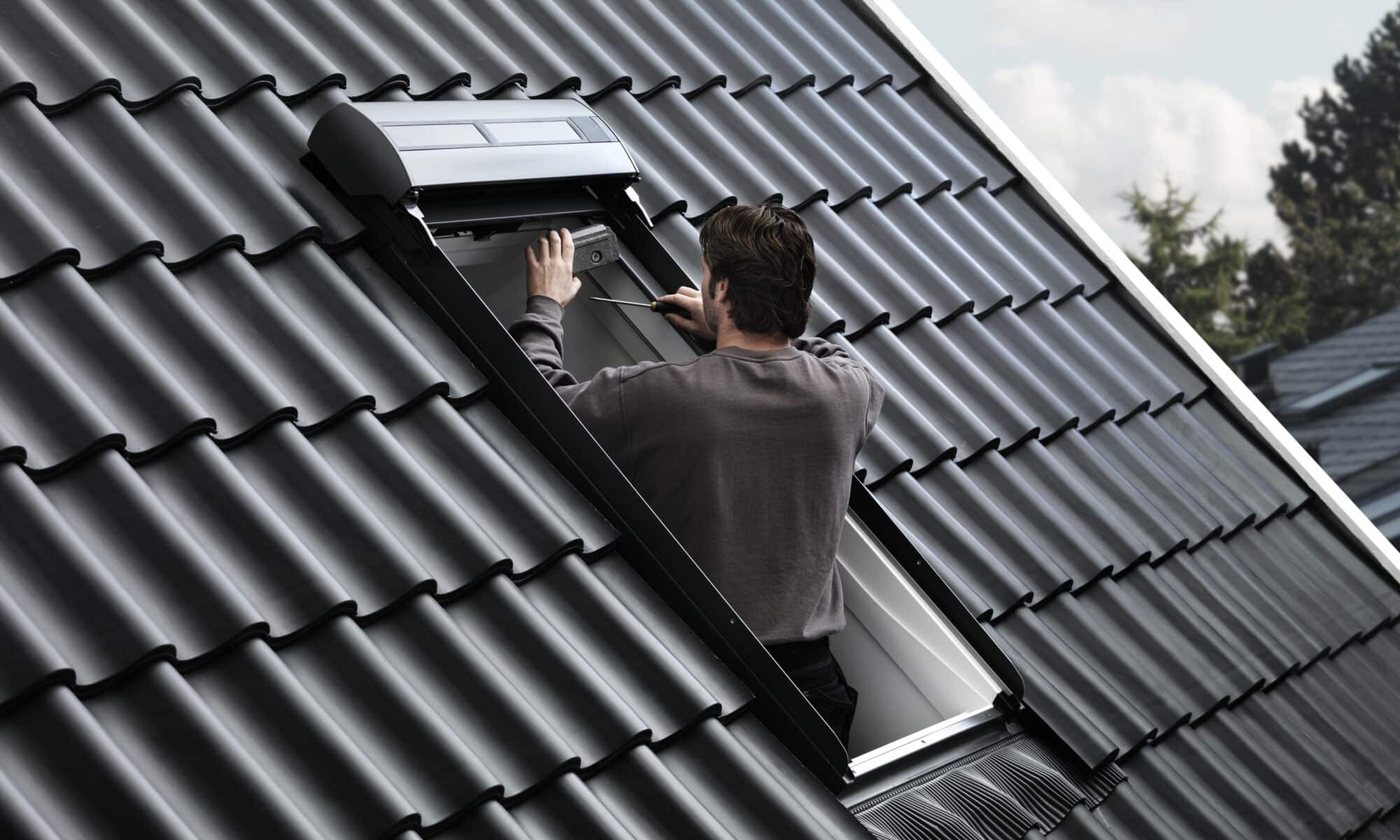 Un homme ajuste une fenêtre de toit VELUX ouverte sur un toit en tuiles.