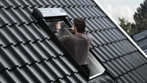 Un homme ajuste une fenêtre de toit VELUX ouverte sur un toit en tuiles.