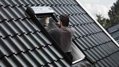 Un homme ajuste une fenêtre de toit VELUX ouverte sur un toit en tuiles.