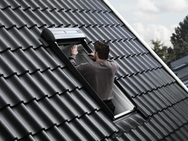 Un homme ajuste une fenêtre de toit VELUX ouverte sur un toit en tuiles.