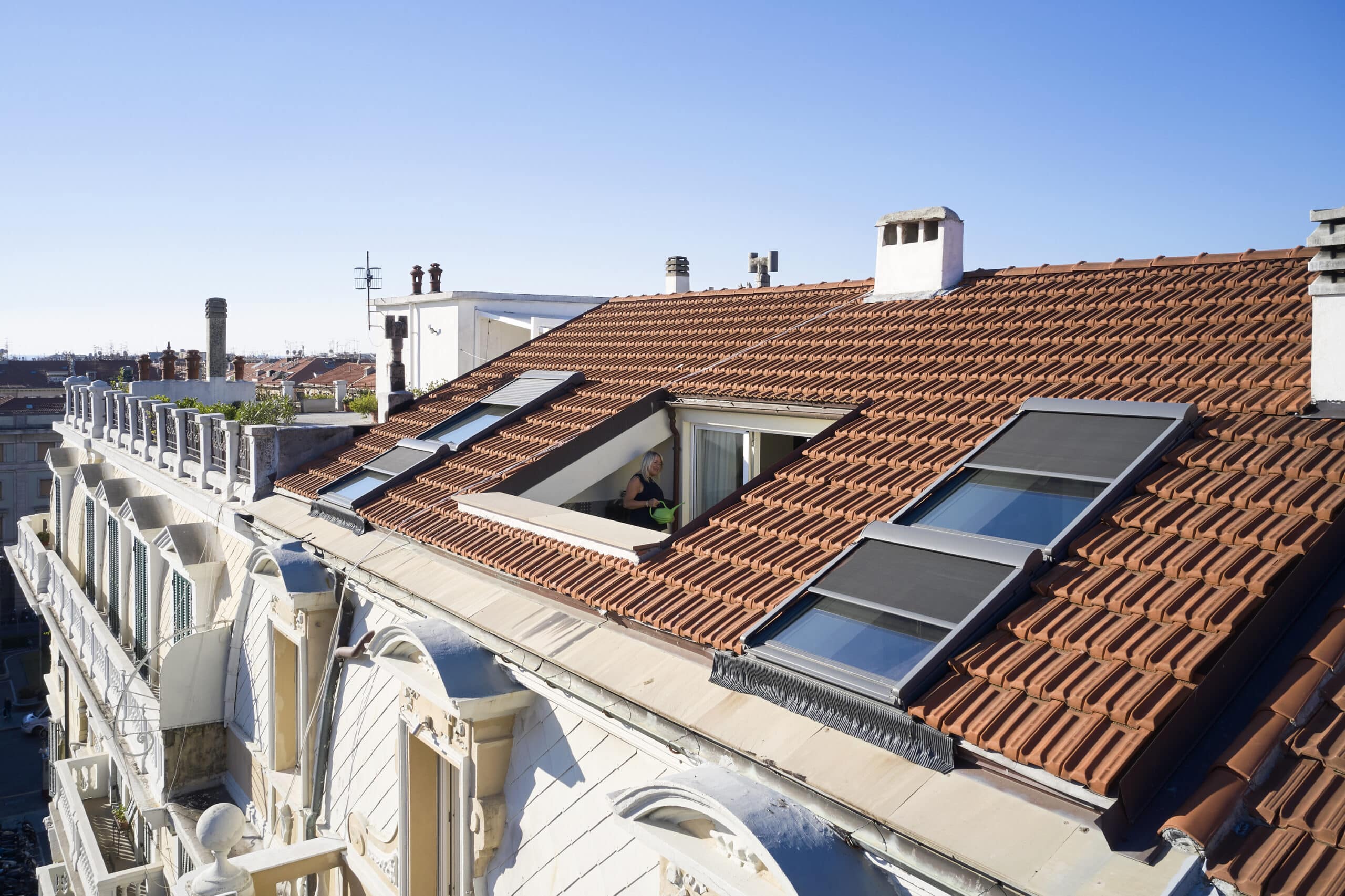 Terrasse sur le toit avec fenêtres VELUX et toit de tuiles rouges, vue sur la ville.