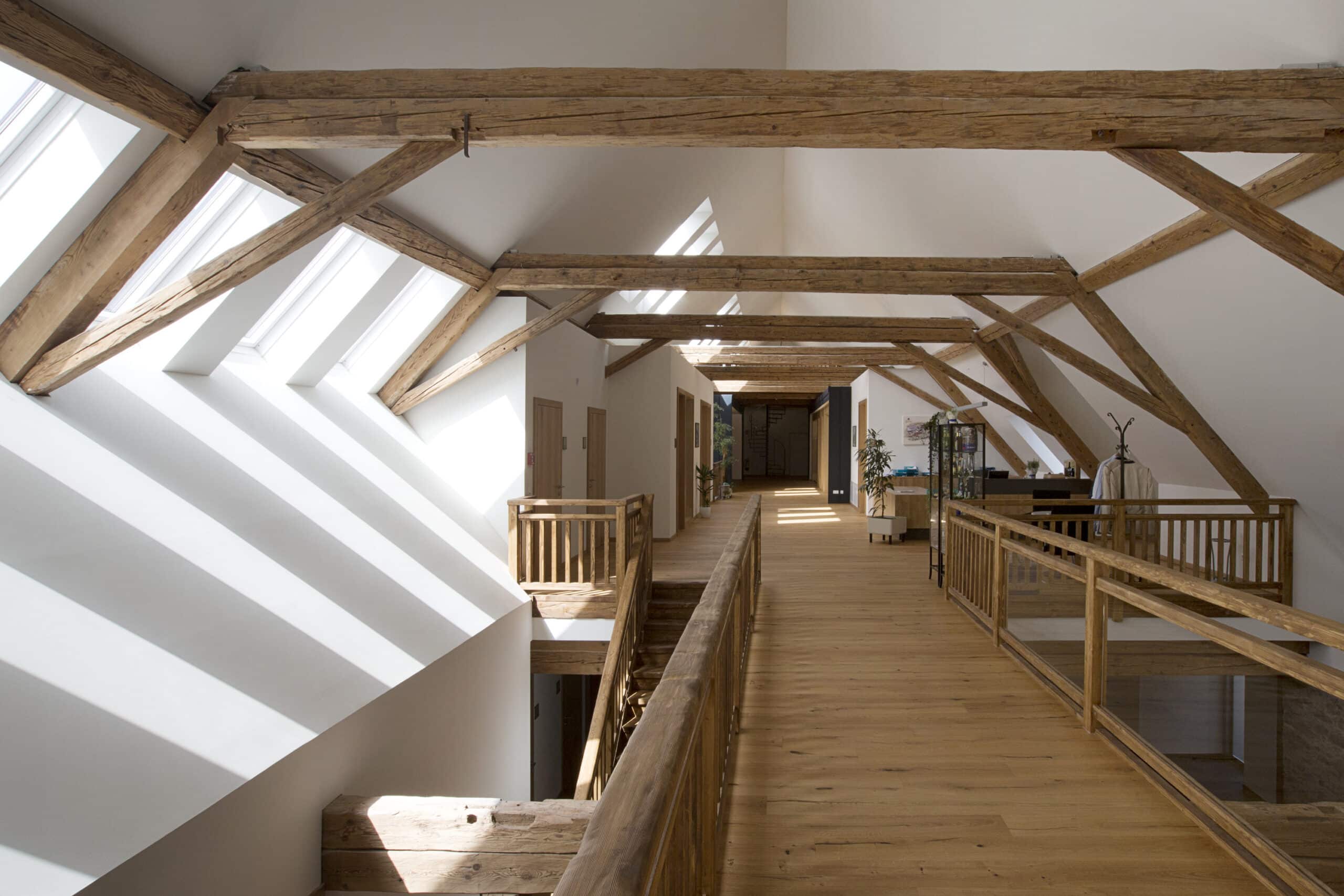 Couloir mansard&eacute; avec plafond en pente, poutres apparentes et fen&ecirc;tres de toit VELUX.