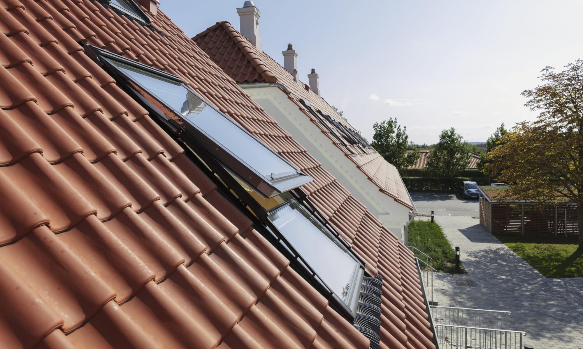 Toit en tuiles rouges avec fenêtres VELUX ouvertes, entouré de verdure.