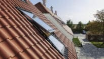 Toit en tuiles rouges avec fenêtres VELUX ouvertes, entouré de verdure.