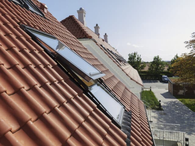 Toit en tuiles rouges avec fenêtres VELUX ouvertes, entouré de verdure.