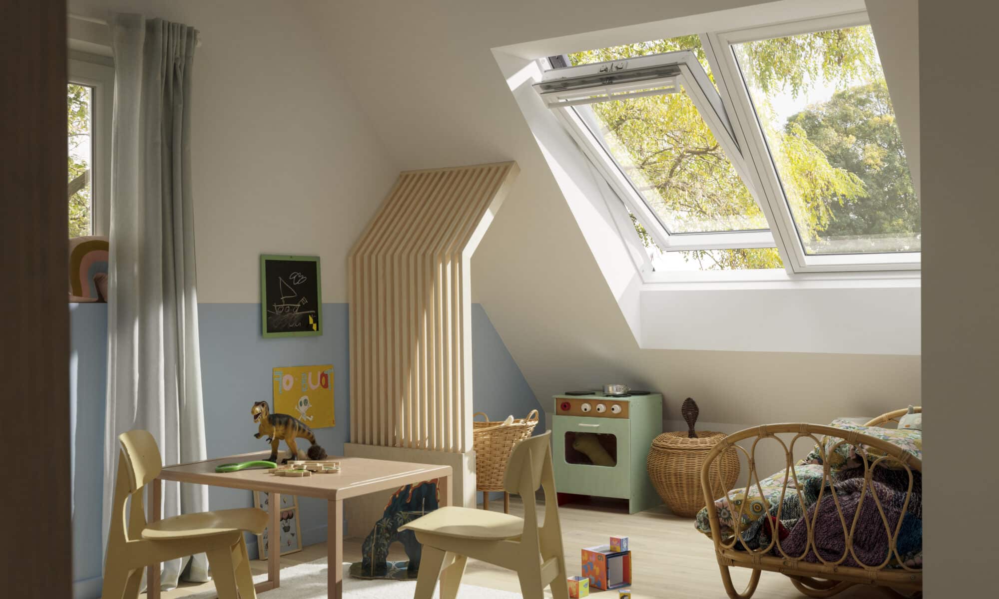 Chambre d'enfant mansardée avec plafond en pente et fenêtre de toit VELUX, remplie de jouets.