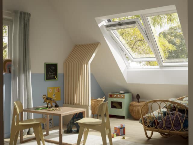 Chambre d'enfant mansardée avec plafond en pente et fenêtre de toit VELUX, remplie de jouets.