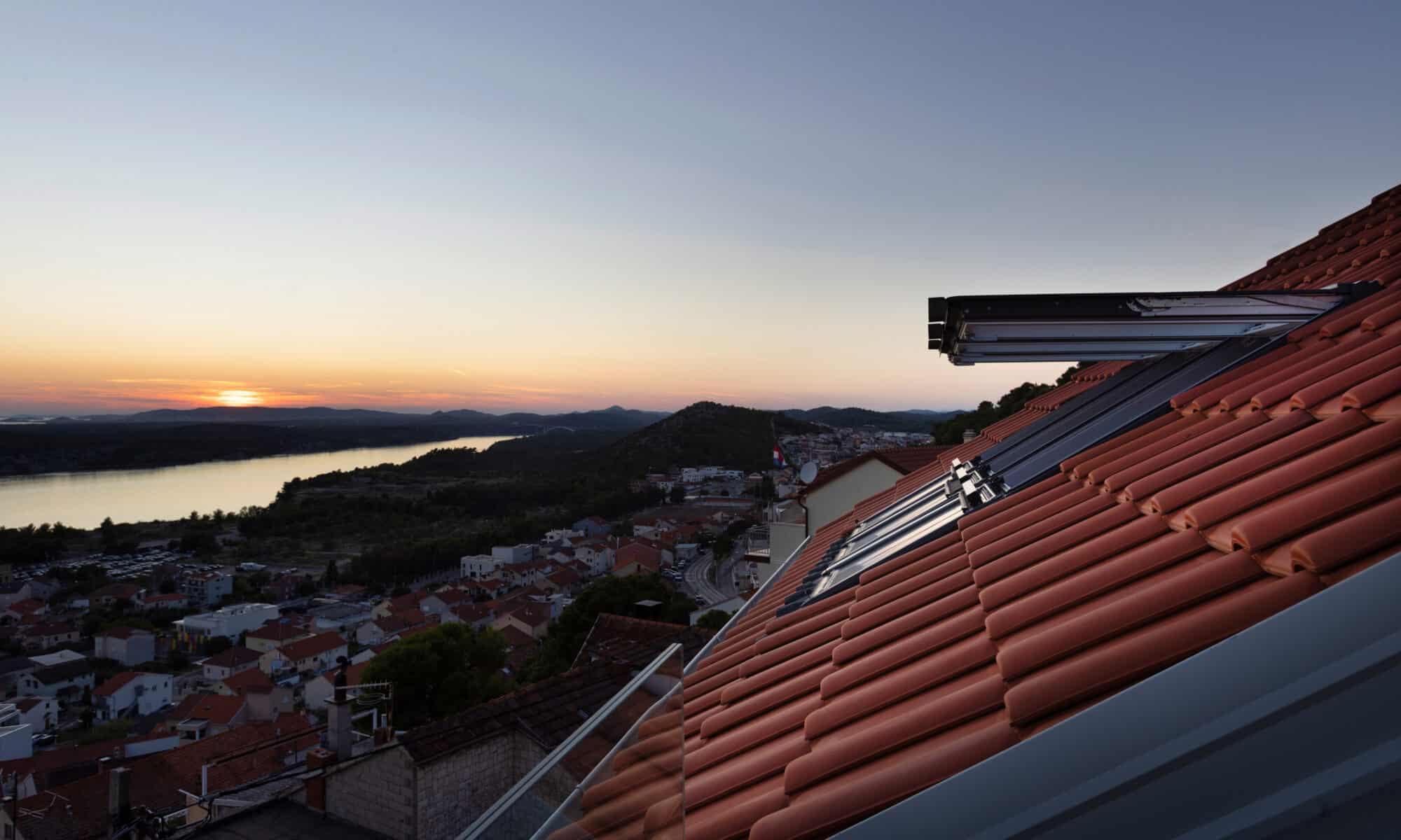 Vue depuis le toit avec les fenêtres de toit VELUX ouvertes au coucher du soleil.