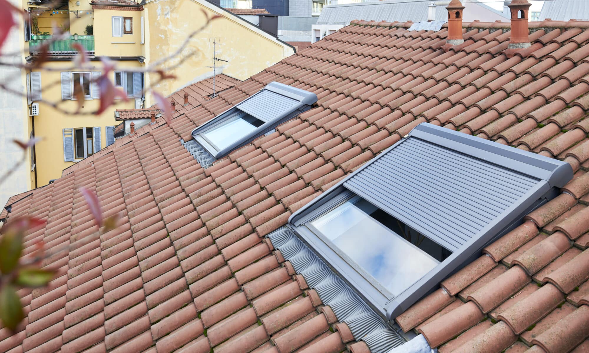 Toiture en tuiles rouges avec deux fenêtres de toit VELUX partiellement ouvertes.