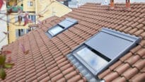 Toiture en tuiles rouges avec deux fenêtres de toit VELUX partiellement ouvertes.