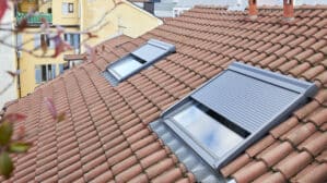 Toiture en tuiles rouges avec deux fenêtres de toit VELUX partiellement ouvertes.