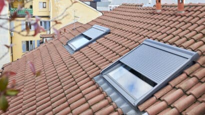 Toiture en tuiles rouges avec deux fenêtres de toit VELUX partiellement ouvertes.
