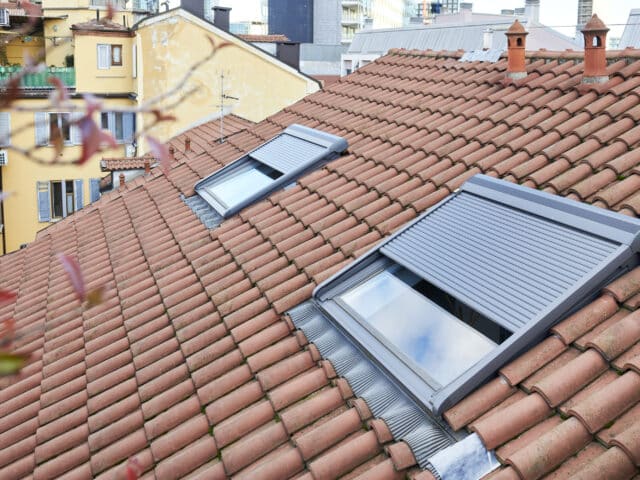 Toiture en tuiles rouges avec deux fenêtres de toit VELUX partiellement ouvertes.
