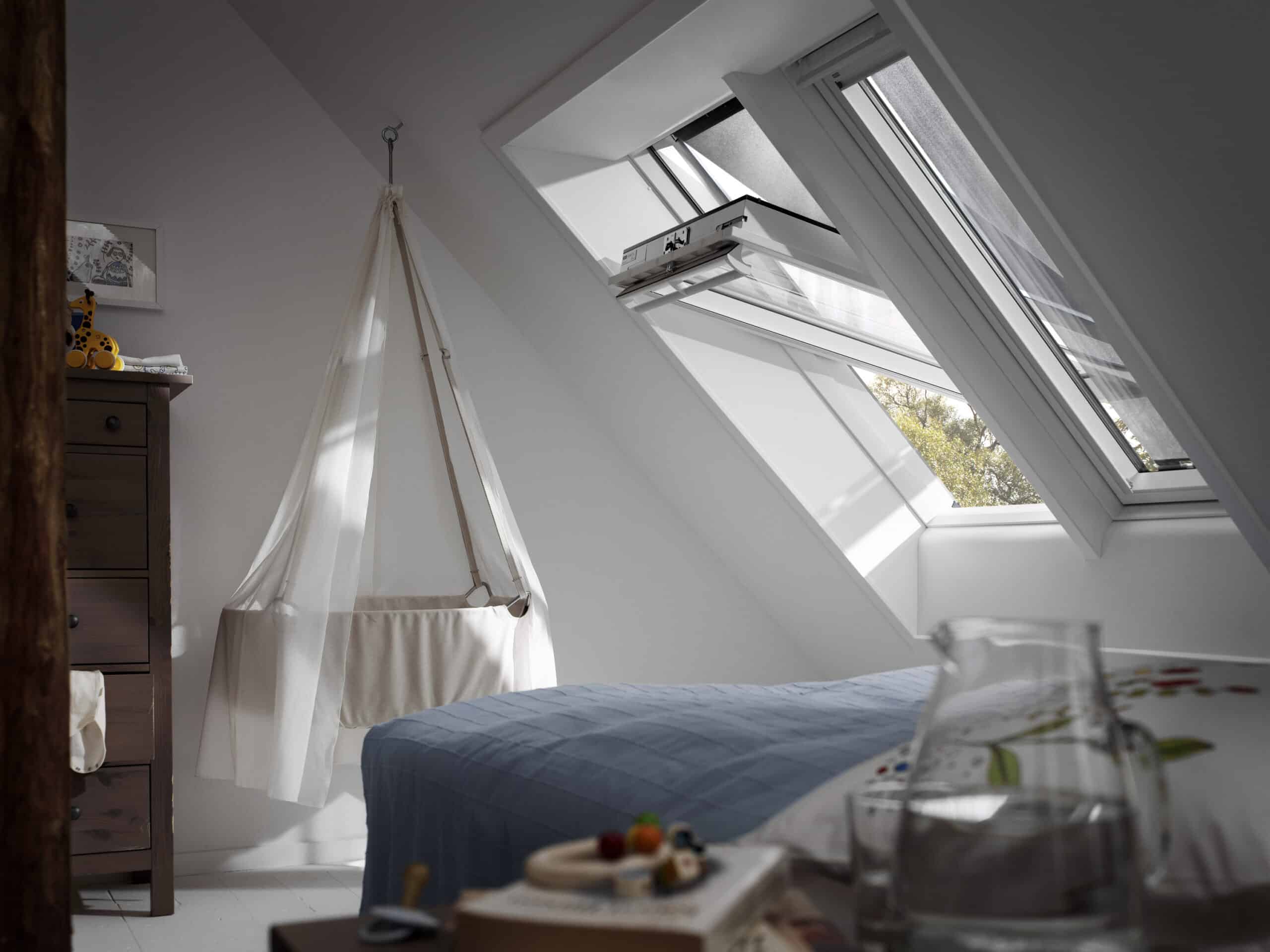 Chambre mansardée avec plafond en pente et fenêtre de toit VELUX ouverte.