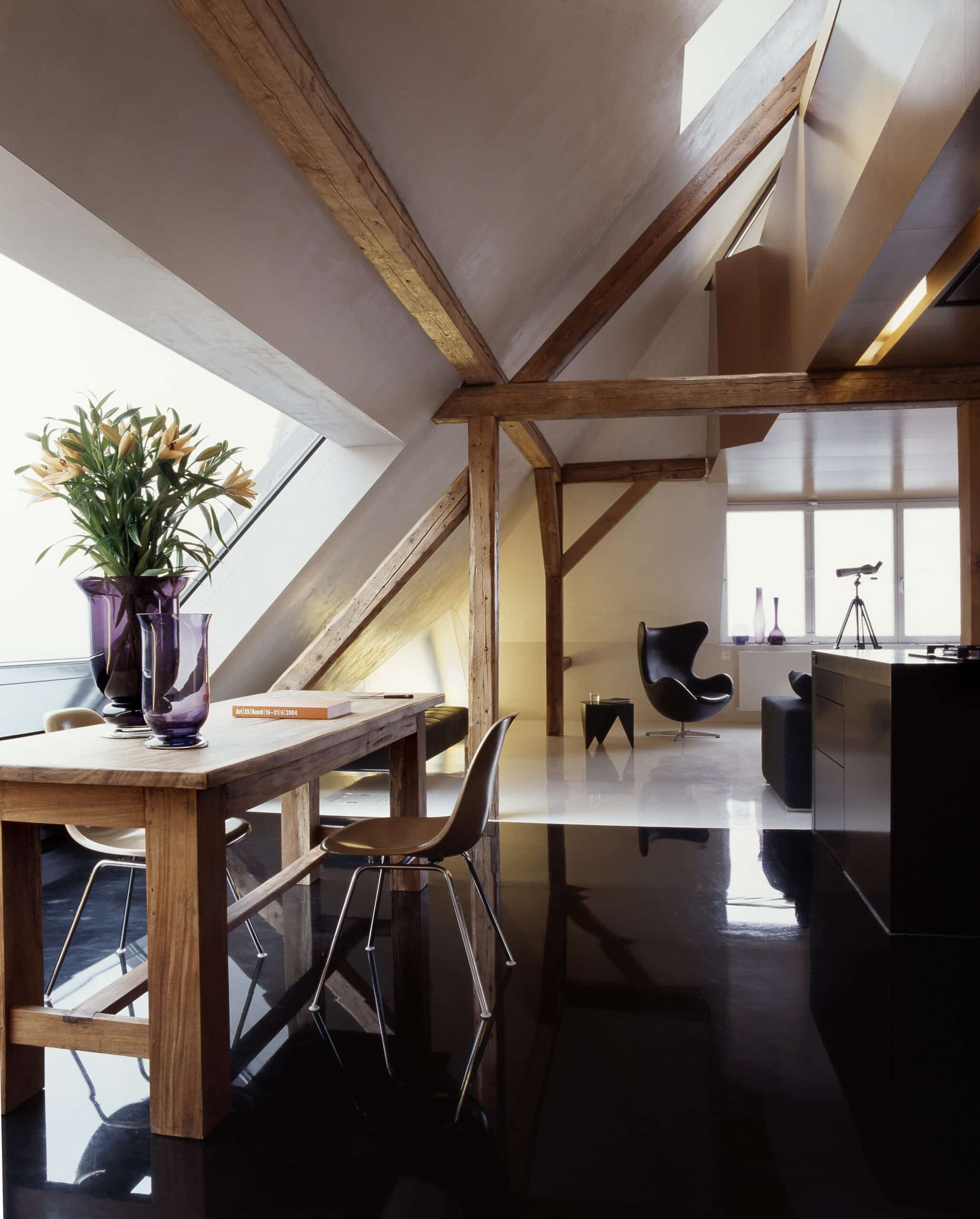 Espace de vie sous combles avec plafond en pente, poutres apparentes en bois et fen&ecirc;tre de toit VELUX.