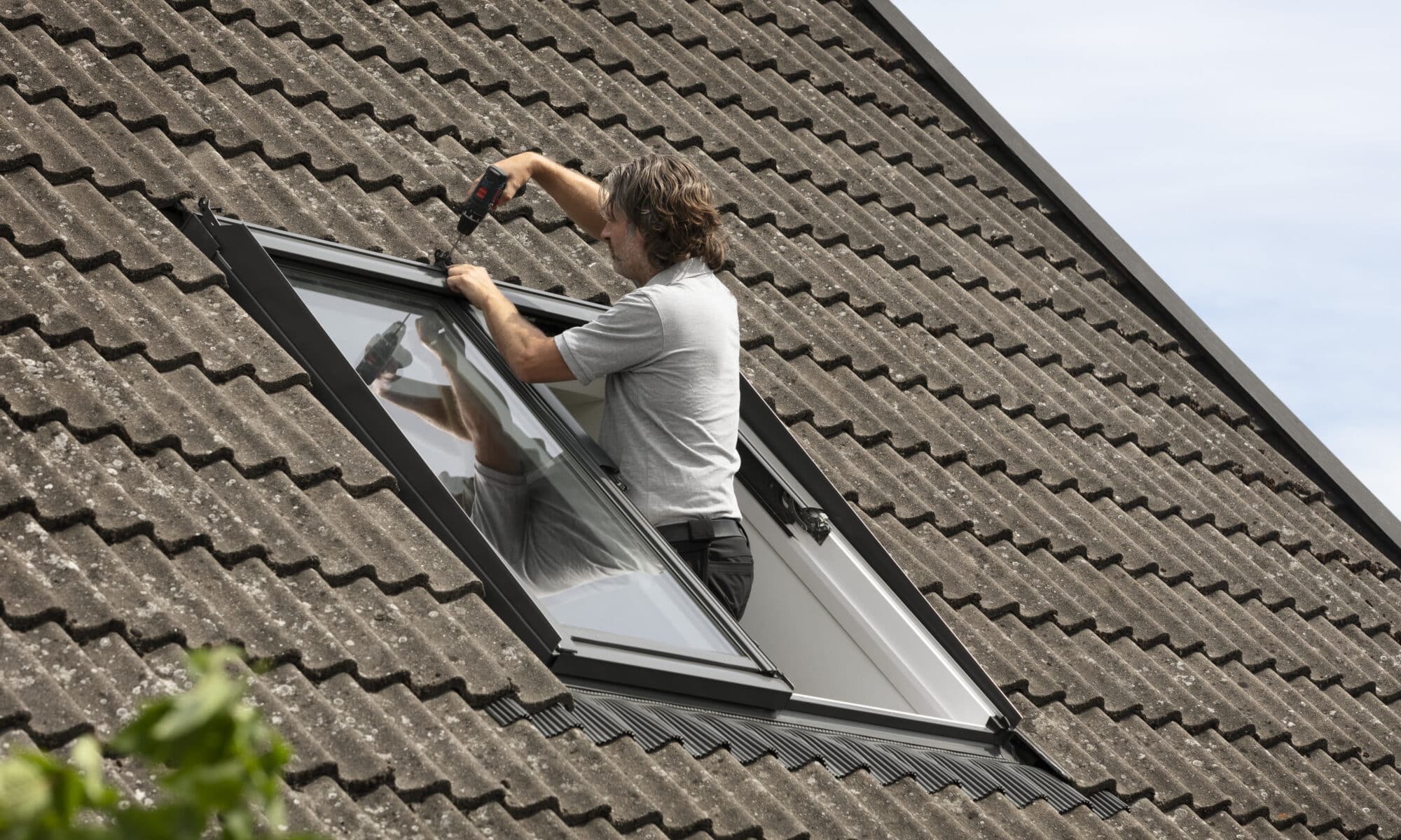 Installation d'une fenêtre de toit VELUX sur un toit en tuiles à forte pente.
