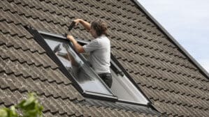 Installation d'une fenêtre de toit VELUX sur un toit en tuiles à forte pente.