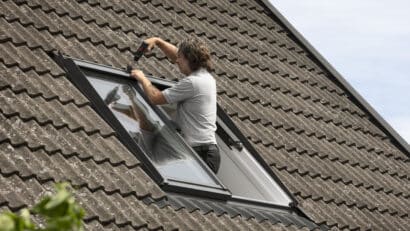 Installation d'une fenêtre de toit VELUX sur un toit en tuiles à forte pente.