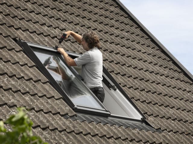Installation d'une fenêtre de toit VELUX sur un toit en tuiles à forte pente.
