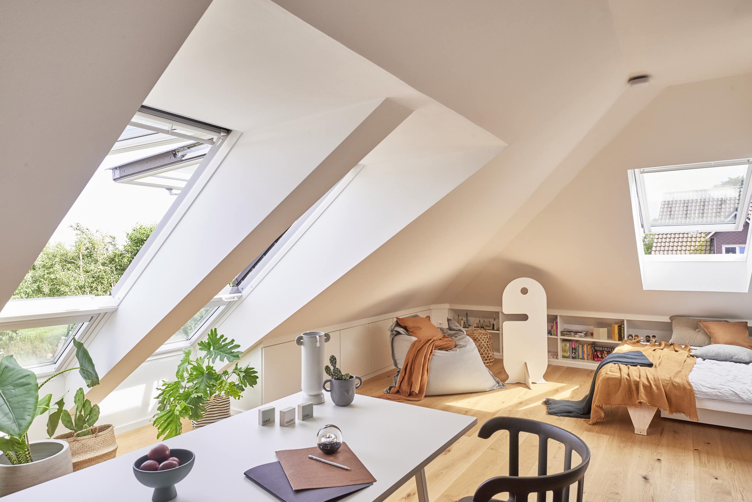 Chambre mansardée avec plafond en pente et fenêtres de toit VELUX ouvertes, décoration chaleureuse.