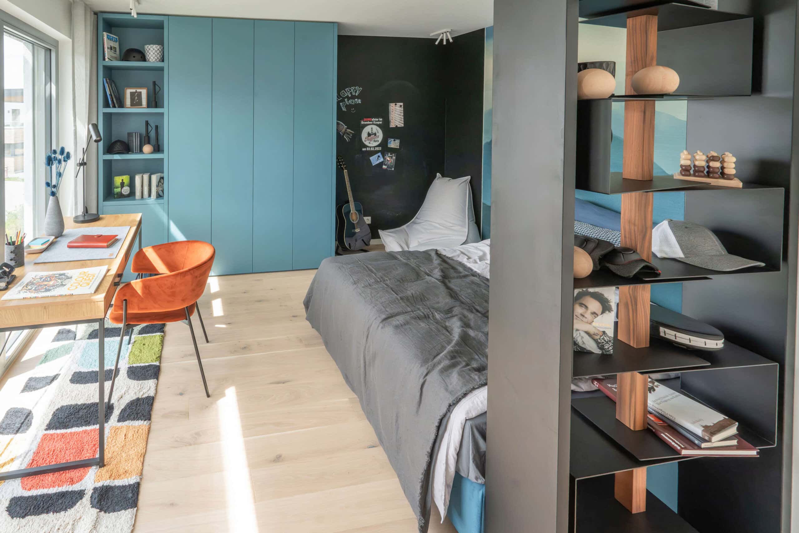 Chambre d'adolescent avec lit, bureau, étagères et guitare, lumineuse et bien organisée.