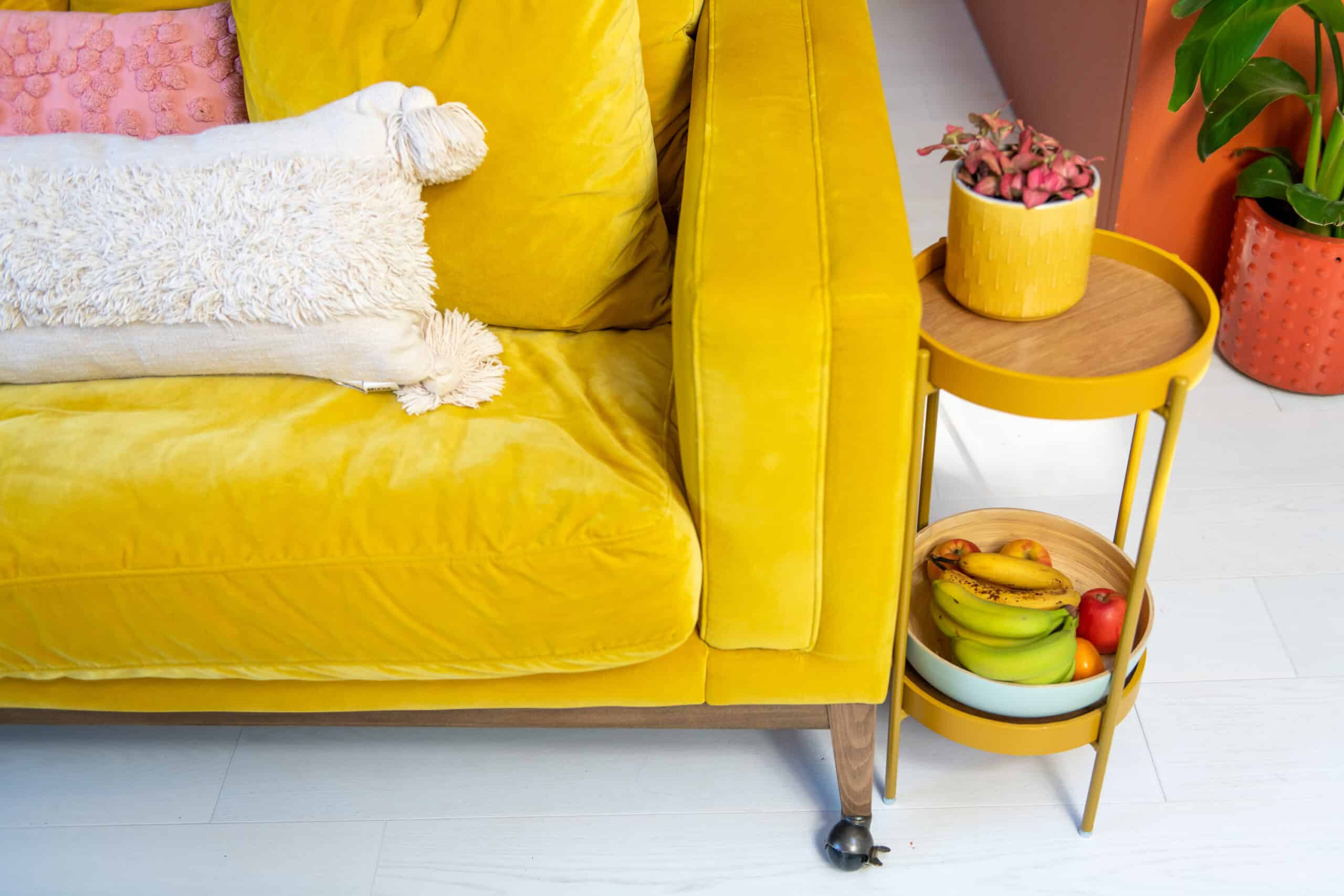 Canapé jaune avec des coussins, table d'appoint avec une plante et des fruits dans le salon.