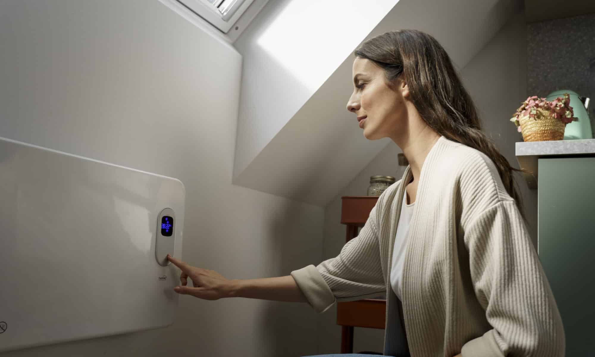 Chambre sous les combles avec plafond en pente et fenêtre de toit VELUX, personne réglant un panneau chauffant