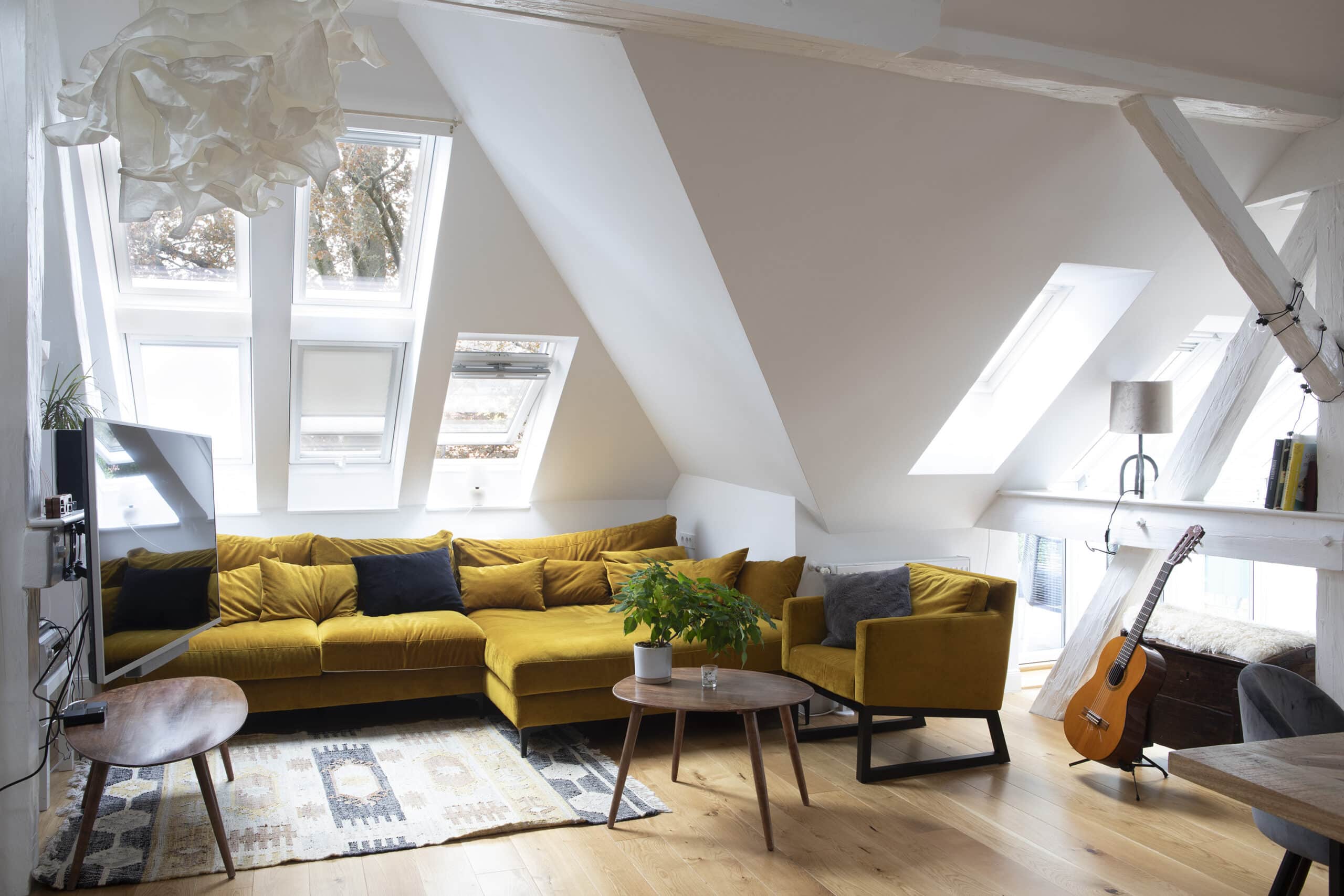 Salon mansardé avec plafond en pente, canapé jaune et fenêtres de toit VELUX.