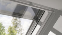 Fenêtre de toit VELUX légèrement entrouverte, vue sur les arbres et le ciel à l'extérieur.