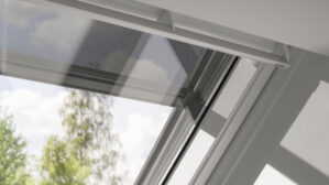 Fenêtre de toit VELUX légèrement entrouverte, vue sur les arbres et le ciel à l'extérieur.