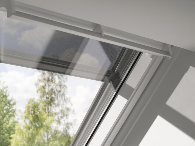 Fenêtre de toit VELUX légèrement entrouverte, vue sur les arbres et le ciel à l'extérieur.