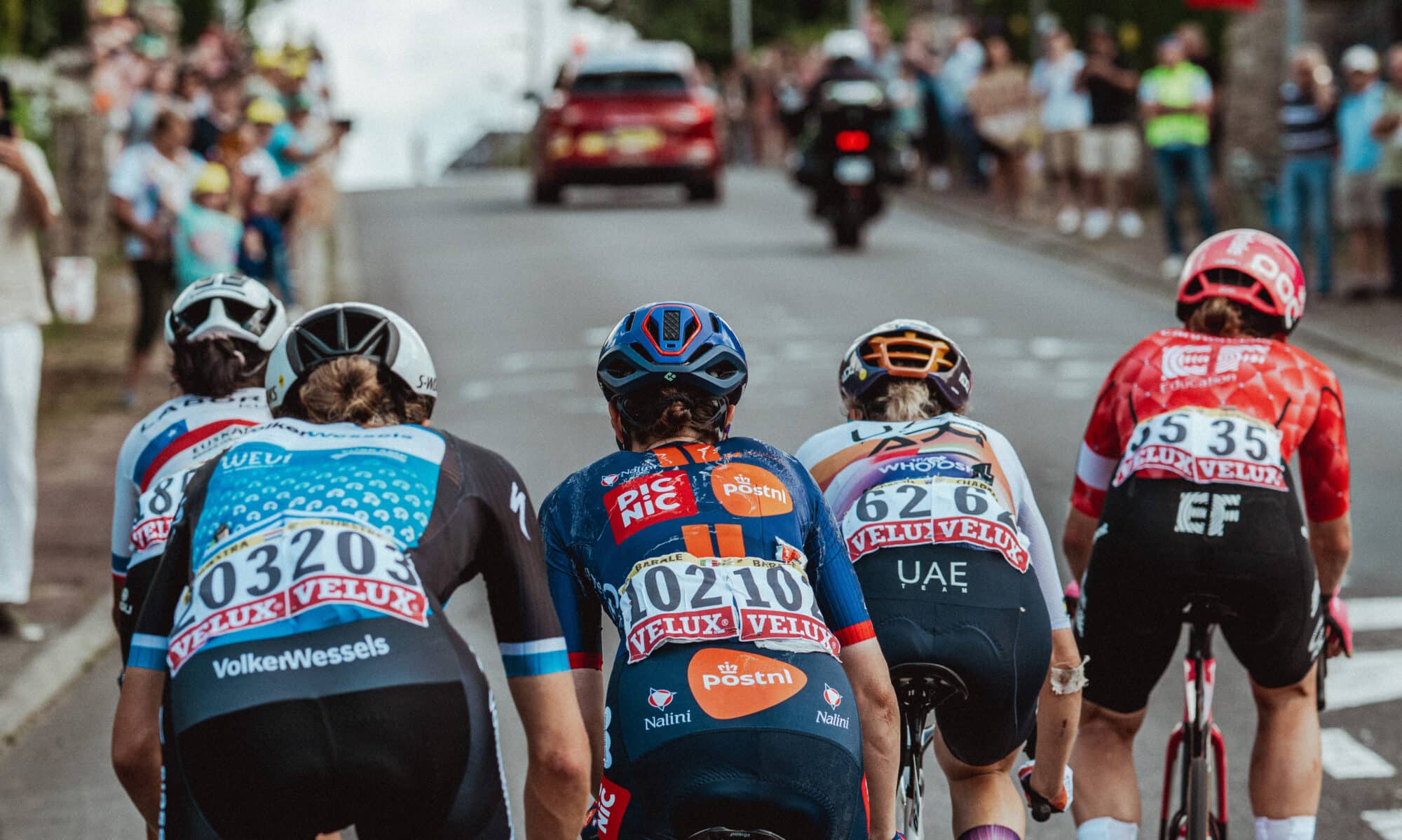 Des cyclistes femmes qui gravissent la côte à toute vitesse, vêtus de maillots colorés et coiffés de casques.