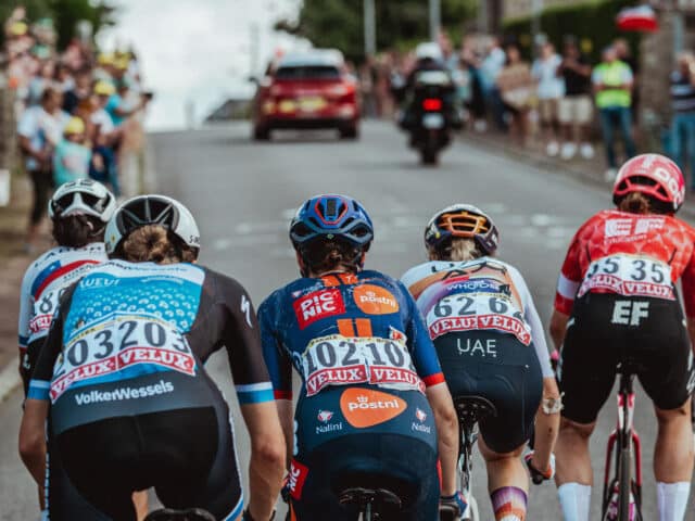 Des cyclistes femmes qui gravissent la côte à toute vitesse, vêtus de maillots colorés et coiffés de casques.
